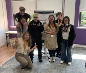 Create Paisley team members standing indoors with a group of young people in front of a flip chart featuring a drawing of a person.