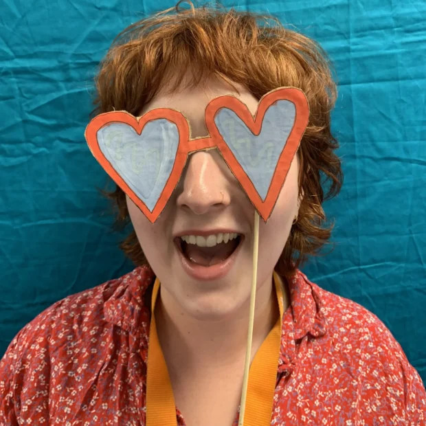 Smiling person wearing handmade, oversized heart-shaped sunglasses